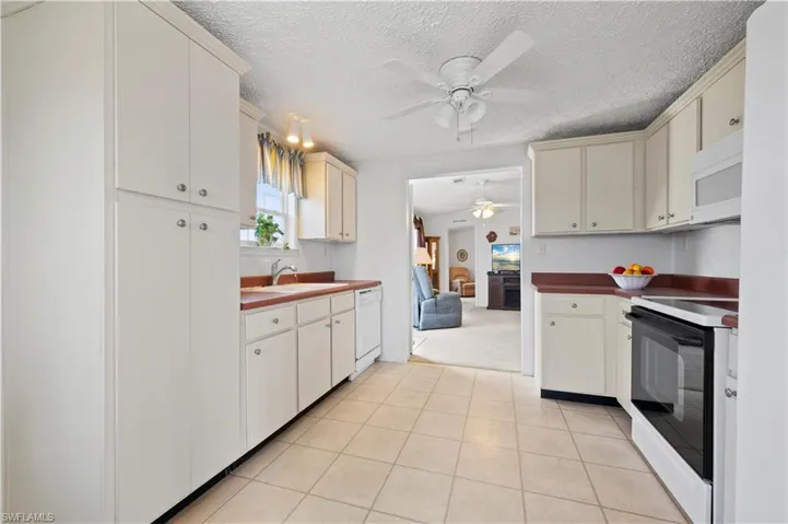 Kitchen featuring white appliances, a textured ceiling, light tile flooring, and ceiling fan