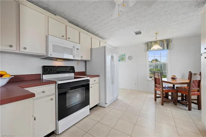 Kitchen with cream cabinetry, white appliances, a textured ceiling, and pendant lighting