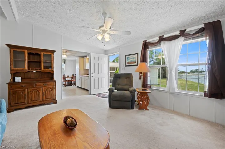 Carpeted living room with a textured ceiling, lofted ceiling, and ceiling fan