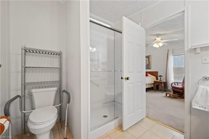 Bathroom featuring ceiling fan, a shower with door, a textured ceiling, tile floors, and toilet
