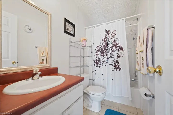 Full bathroom featuring vanity with extensive cabinet space, a textured ceiling, shower / tub combo with curtain, tile floors, and toilet