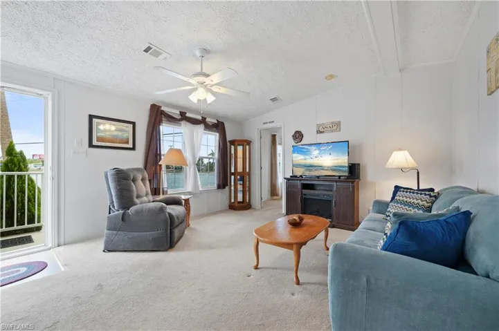 Living room featuring a textured ceiling, ceiling fan, vaulted ceiling, and light colored carpet