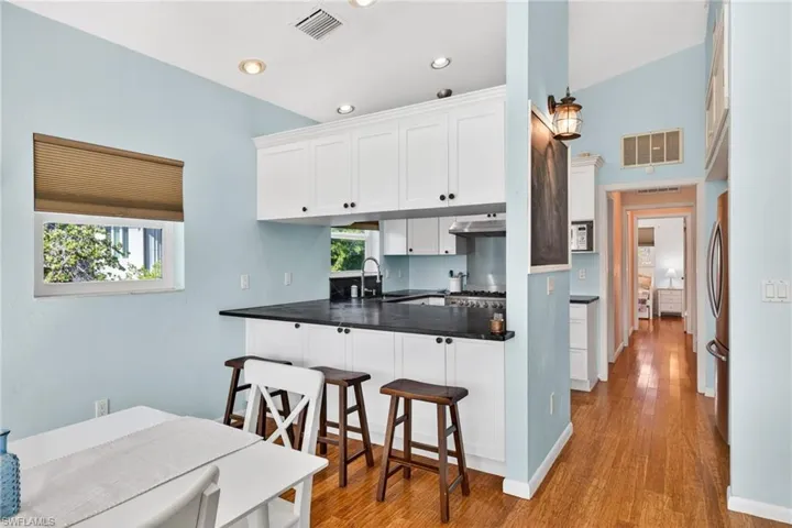 Kitchen with white cabinetry, dark countertops, a kitchen breakfast bar, wood finished floors, and a peninsula