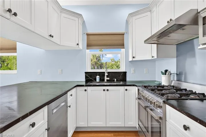 Kitchen featuring stainless steel appliances, dark countertops, under cabinet range hood, and white cabinets