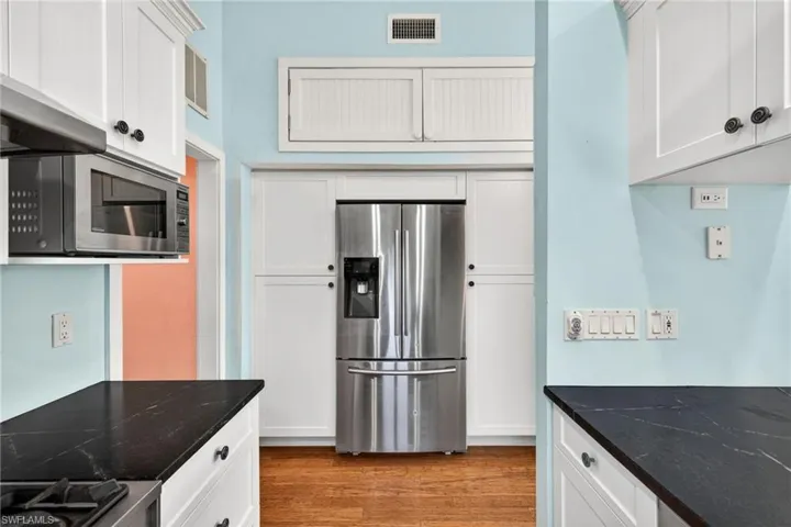 Kitchen featuring stainless steel appliances, white cabinets, light wood-style flooring, and dark stone countertops
