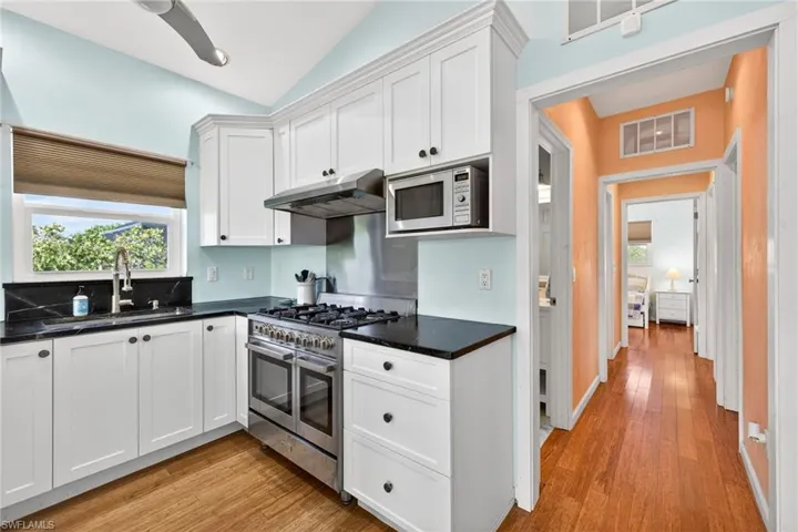 Kitchen featuring white cabinetry, stainless steel appliances, under cabinet range hood, light wood finished floors, and lofted ceiling