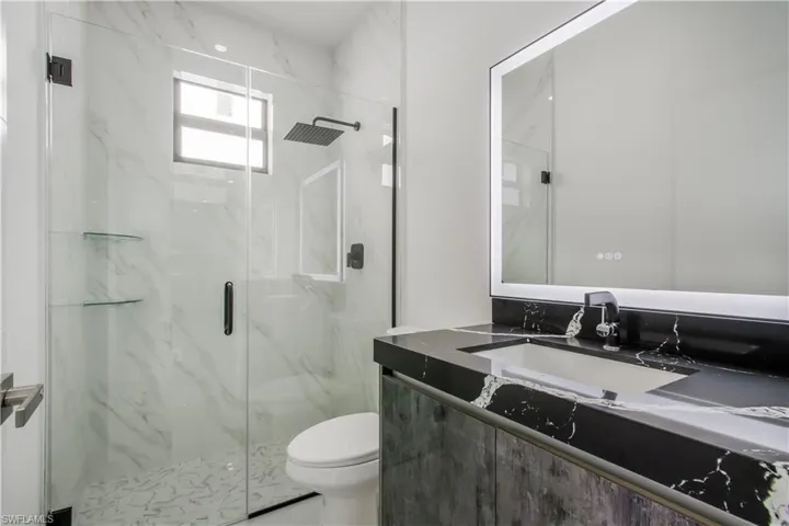 Full bath with a marble finish shower, toilet, and vanity