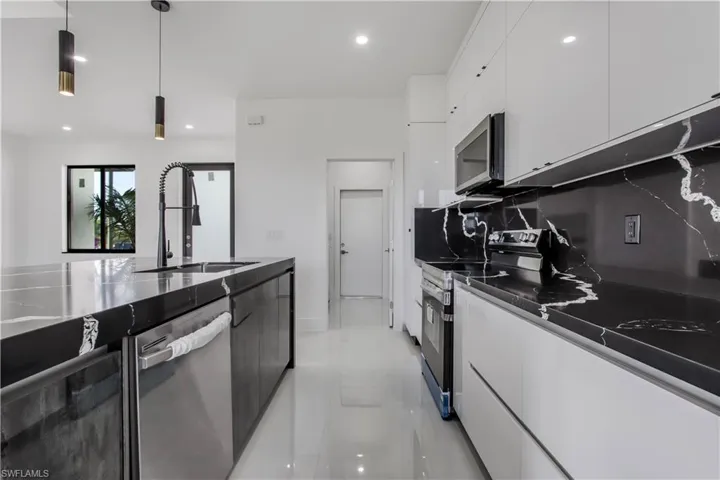 Kitchen with a sink, decorative backsplash, appliances with stainless steel finishes, white cabinetry, and modern cabinets