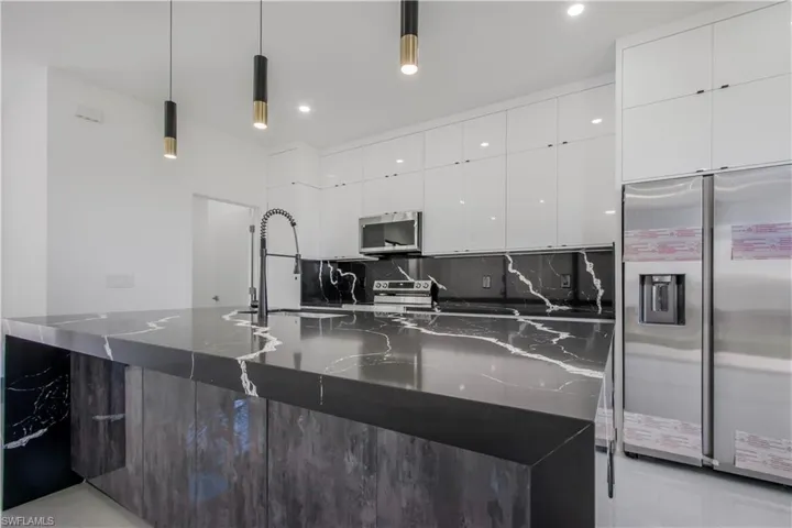 Kitchen featuring dark stone countertops, decorative backsplash, white cabinets, appliances with stainless steel finishes, and modern cabinets