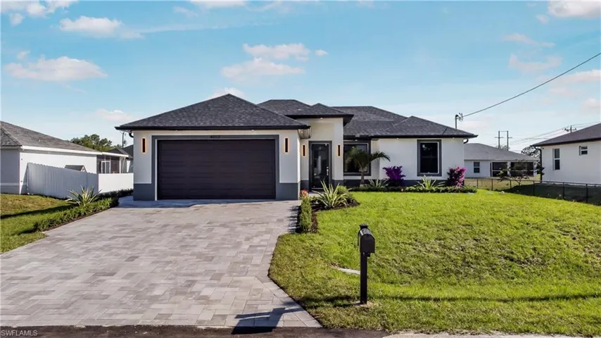 View of front of house featuring stucco siding, decorative driveway, a front lawn, and fence