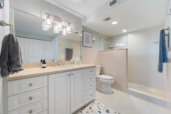 Bathroom with vanity, tiled shower, tile walls, tile patterned flooring, and toilet