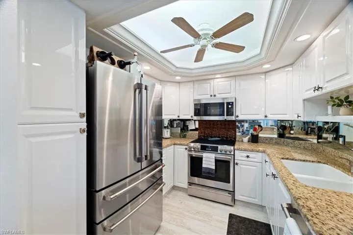 Kitchen featuring light stone countertops, white cabinetry, stainless steel appliances, and a tray ceiling