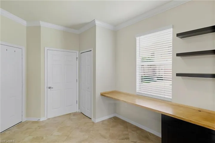 Unfurnished office featuring built in desk and crown molding