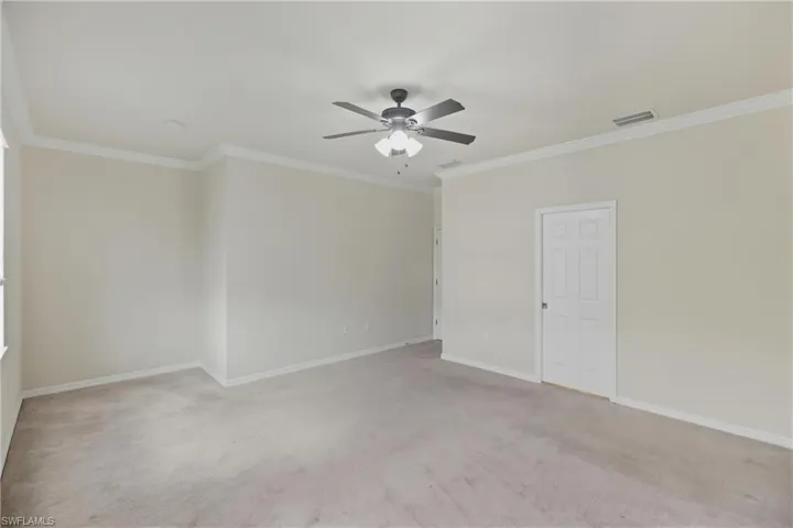 Empty room with ornamental molding, light colored carpet, and ceiling fan
