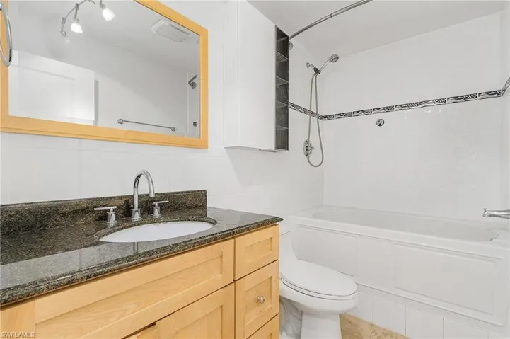 Full bathroom featuring toilet, tile walls, tasteful backsplash, large vanity, and tiled shower / bath combo