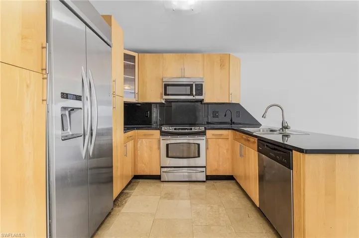 Kitchen featuring light brown cabinetry, backsplash, light tile floors, sink, and appliances with stainless steel finishes