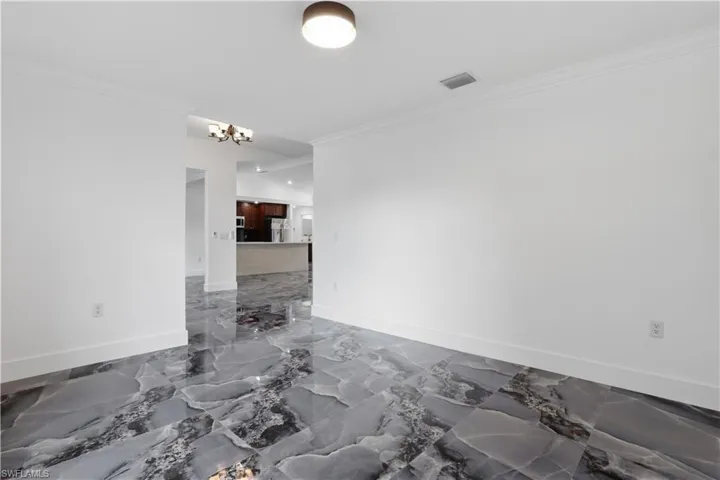 Unfurnished room featuring ornamental molding, dark marble finish flooring, and a chandelier