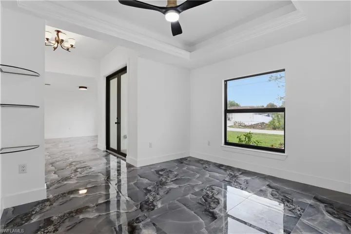 Spare room with dark marble finish floors, ceiling fan, a raised ceiling, suspended lighting, and ornamental molding
