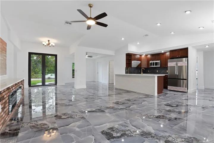 Unfurnished living room with ceiling fan, light marble finish floors, and vaulted ceiling
