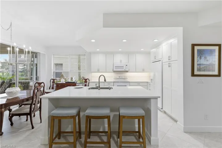 Kitchen featuring white cabinets, a breakfast bar, recessed lighting, white appliances, and light tile patterned flooring