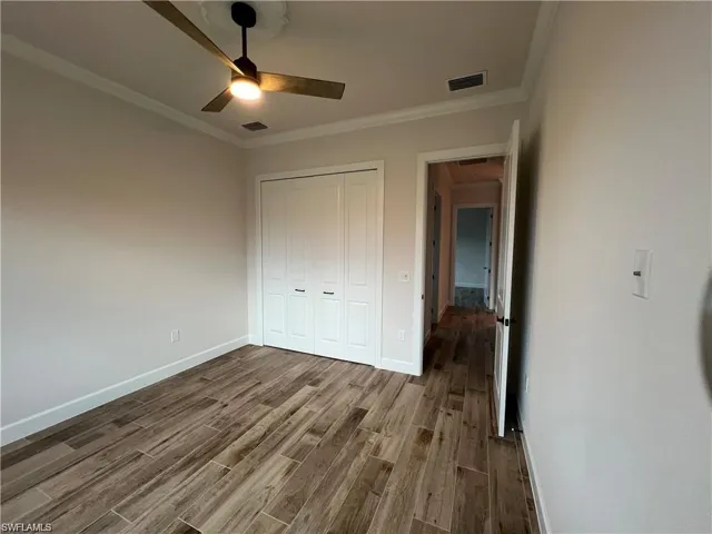 Unfurnished bedroom with a closet, hardwood / wood-style flooring, ceiling fan, and crown molding