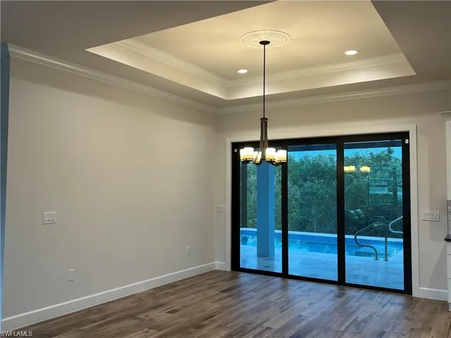 Spare room with ornamental molding, wood-type flooring, a tray ceiling, and a notable chandelier