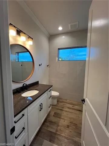 Bathroom with ornamental molding, wood-type flooring, vanity, and toilet
