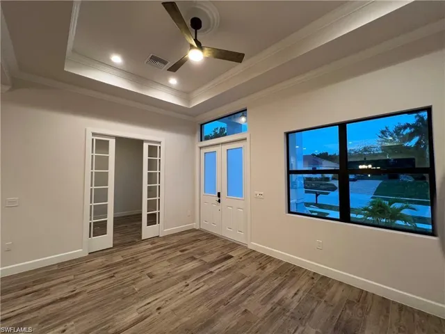 Unfurnished room with a tray ceiling, hardwood / wood-style floors, crown molding, ceiling fan, and french doors
