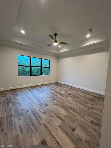 Empty room featuring ornamental molding, a tray ceiling, hardwood / wood-style floors, and ceiling fan