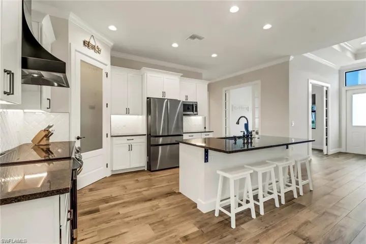 Kitchen with a center island with sink, wall chimney exhaust hood, white cabinetry, appliances with stainless steel finishes, and light hardwood / wood-style floors