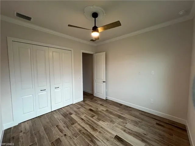 Unfurnished bedroom with ceiling fan, a closet, hardwood / wood-style floors, and ornamental molding