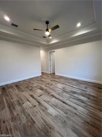 Empty room with ceiling fan, a raised ceiling, crown molding, and hardwood / wood-style floors