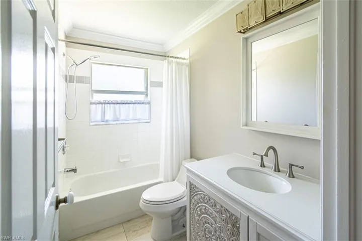 Bathroom featuring a vanity with detailed carved cabinet doors, a solid-surface countertop, an integrated sink, a framed mirror, and a tub-shower combination with tiled surround