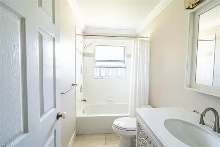 Bathroom featuring a porcelain tub with a tiled surround, a vanity with an integrated basin, a wall-mounted mirror, crown molding, and stone-finish floor tile