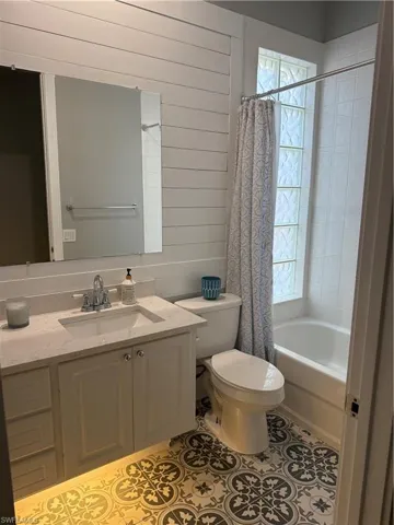 Full bathroom with wood walls, vanity, shower / bath combo, healthy amount of natural light, and light tile patterned floors