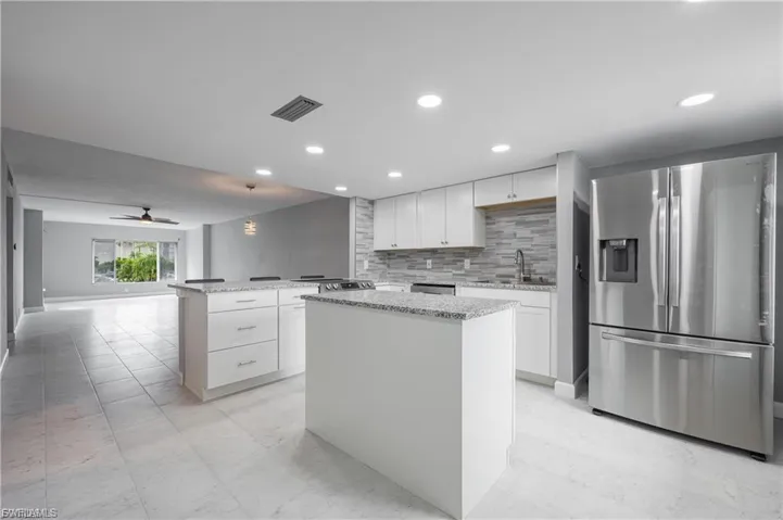 Kitchen featuring white cabinetry, stainless steel refrigerator with ice dispenser, a center island, hanging light fixtures, and light stone counters