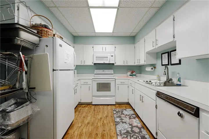 Kitchen with a paneled ceiling, white appliances, white cabinetry, light countertops, and light wood-style flooring