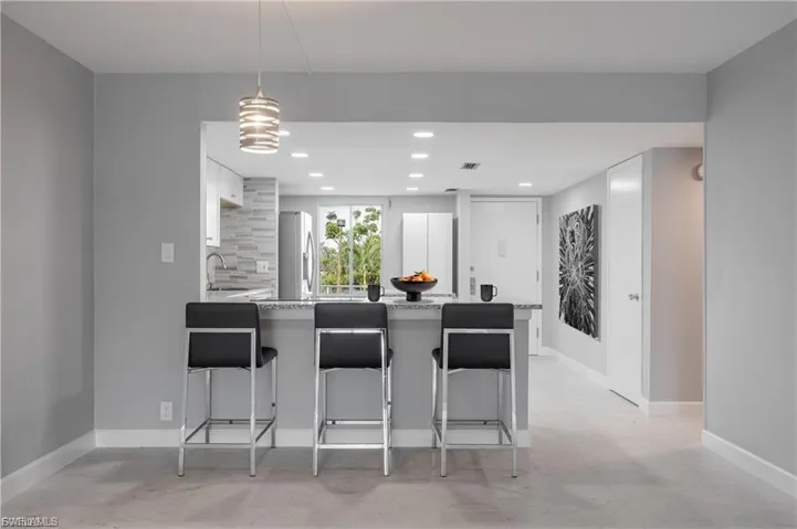 Kitchen featuring a peninsula, light stone counters, a breakfast bar area, freestanding refrigerator, and white cabinetry