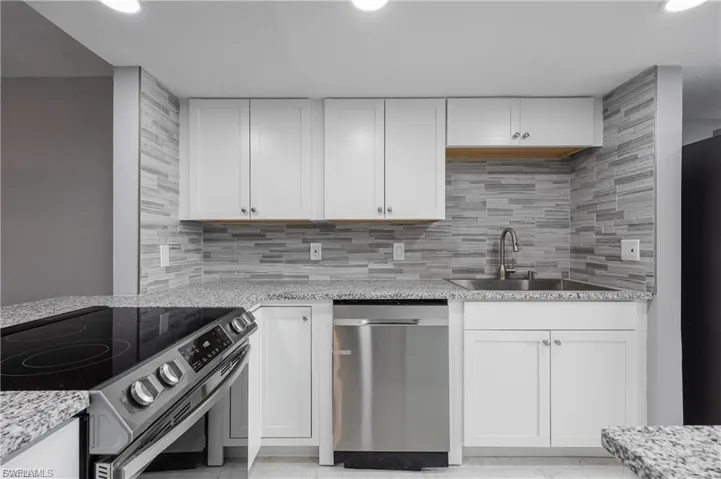Kitchen with appliances with stainless steel finishes, white cabinetry, light stone counters, decorative backsplash, and recessed lighting