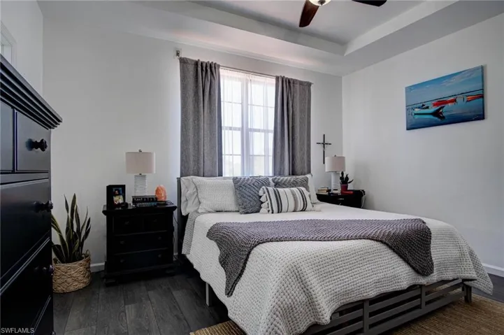 Bedroom featuring a tray ceiling, dark wood-type flooring, and ceiling fan