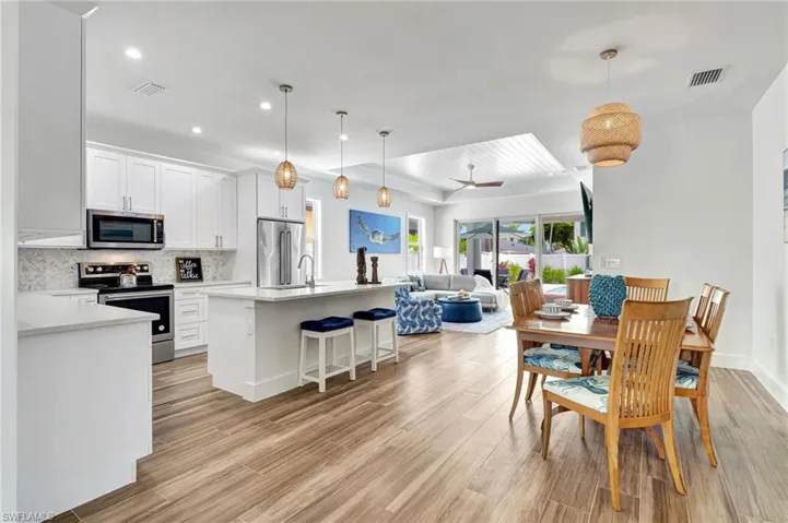 Kitchen with stainless steel appliances, hanging light fixtures, a breakfast bar area, light hardwood / wood-style floors, and backsplash