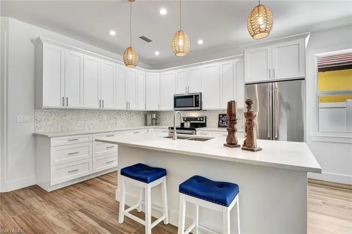 Kitchen featuring white cabinetry, tasteful backsplash, pendant lighting, an island with sink, and appliances with stainless steel finishes
