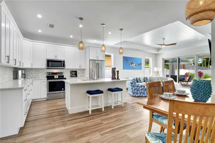 Kitchen with appliances with stainless steel finishes, pendant lighting, decorative backsplash, a kitchen island with sink, and a tray ceiling