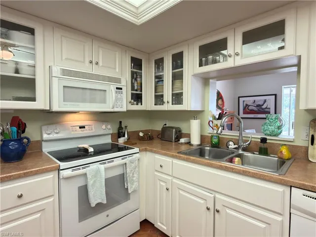 Kitchen featuring white appliances, glass fronted cabinets, and white cabinets