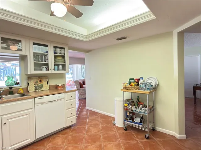 Kitchen featuring glass insert cabinets, dishwasher, light tile patterned flooring, a tray ceiling, and white cabinets