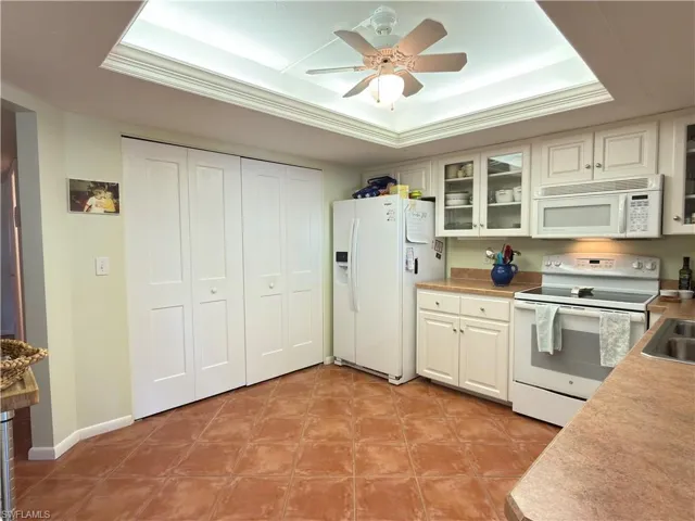 Kitchen with white appliances, light countertops, a tray ceiling, glass insert cabinets, and ceiling fan