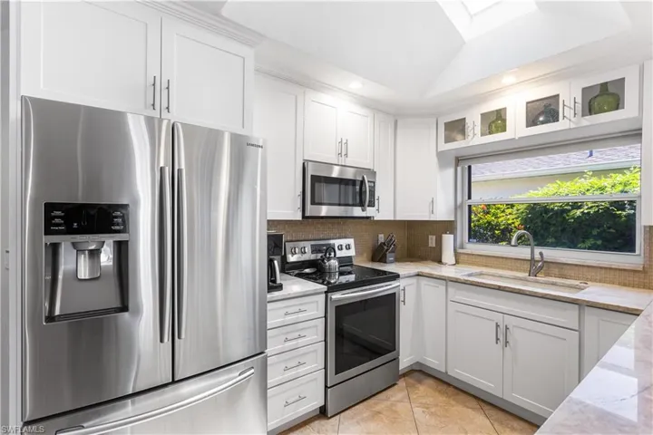 Kitchen with stainless steel appliances, light stone counters, backsplash, sink, and white cabinetry