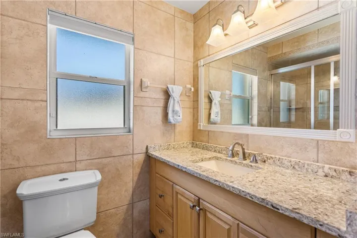 Bathroom featuring tile walls, toilet, and vanity with extensive cabinet space