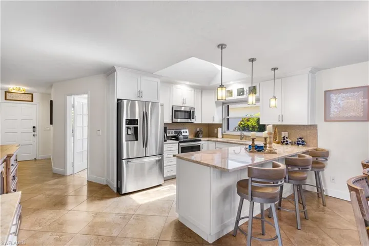Kitchen featuring decorative light fixtures, kitchen peninsula, tasteful backsplash, white cabinetry, and appliances with stainless steel finishes
