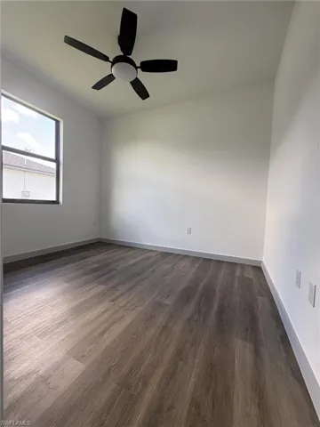 Spacious room featuring wood-finish flooring, a contemporary ceiling fan with integrated lighting, and a large window providing natural light